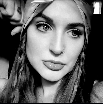 "Picture of Rachel William: a Causcasian woman wearing a bandana and two braids to the front of her long hair.
She is gazing into the distance in this full face photograph.