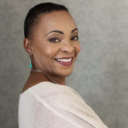 Photo of Sheila Balgobin smiling, an African American woman of medium complexion. She is wearing a top with metallic silver thread, posed with arms crossed and looking at the camera from a side angle - her  head is turned to the right, looking over should