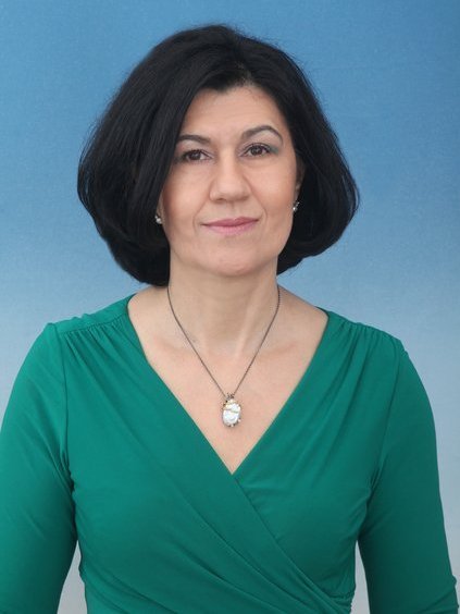 A medium-size, Caucasian woman, with a dark hair and wellfited turcoaze color dress. With symmetrical and bright, smiley face.