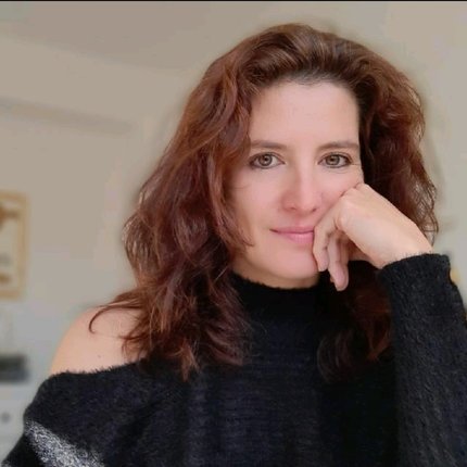 Portrait of Catarina Jessica Keil. A Caucasian woman from European descent with long wavy brown hair wearing a dark woolen top, seated, staring peacefully into the camera.